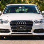 Biały sedan Audi sfotografowany z przodu na parkingu, z widocznym grillem i reflektorami