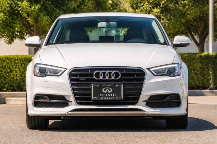 Biały sedan Audi sfotografowany z przodu na parkingu, z widocznym grillem i reflektorami